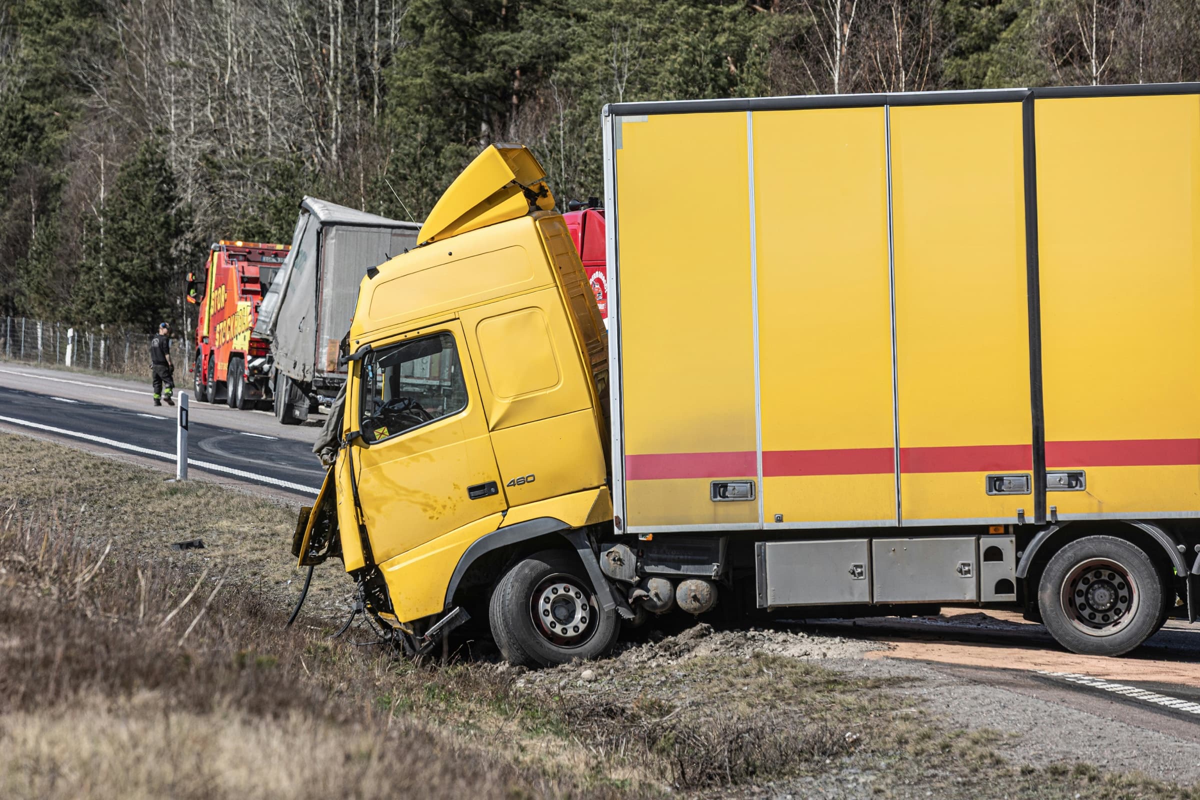 Severely damaged yellow commercial truck after leaving the roadway